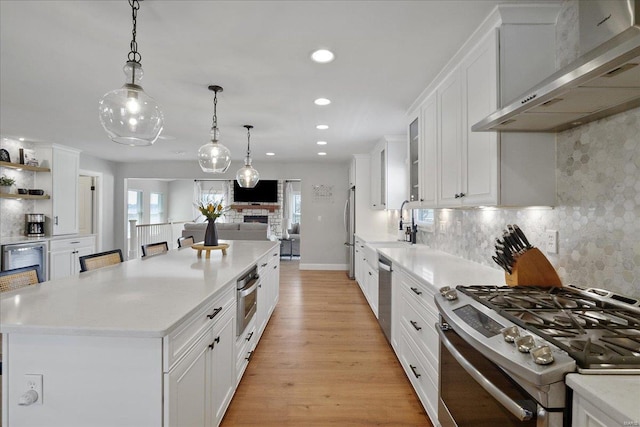 kitchen featuring white cabinetry, stainless steel appliances, wall chimney exhaust hood, and light countertops