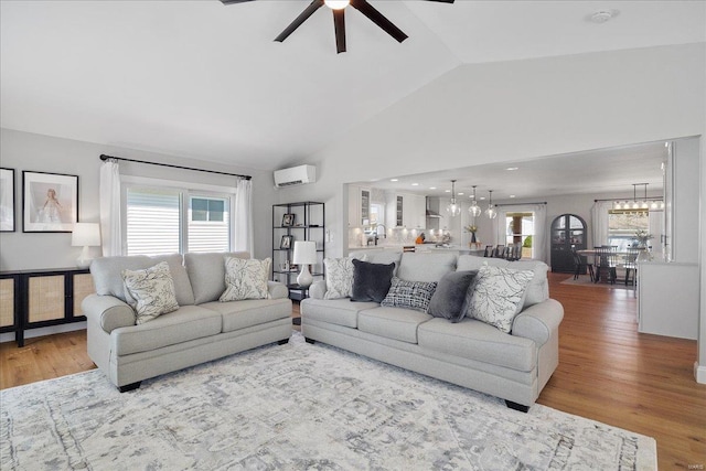 living room with wood finished floors, a wealth of natural light, ceiling fan with notable chandelier, and a wall mounted air conditioner