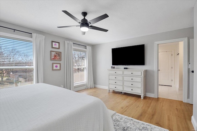 bedroom featuring light wood finished floors, baseboards, a textured ceiling, and a ceiling fan