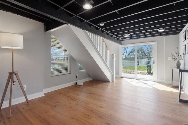 below grade area with baseboards, wood finished floors, and stairs