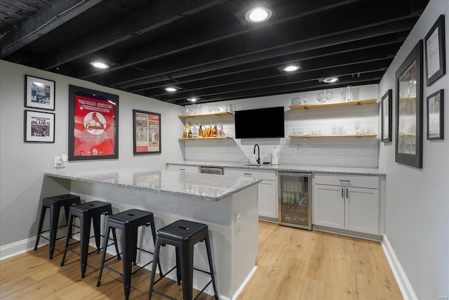 bar featuring beverage cooler, a sink, wet bar, light wood-style floors, and baseboards