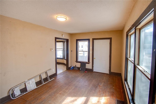 empty room with visible vents, a textured ceiling, baseboards, and wood finished floors