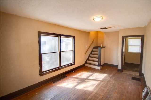 empty room with visible vents, wood-type flooring, plenty of natural light, and stairs