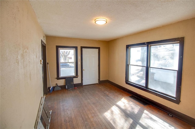 empty room featuring baseboards, visible vents, wood-type flooring, and a textured ceiling