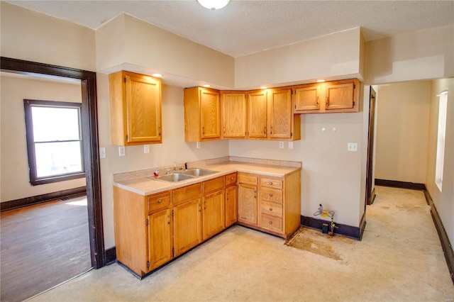 kitchen with brown cabinetry, baseboards, a sink, light countertops, and a textured ceiling