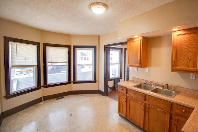 kitchen with visible vents, a sink, a textured ceiling, brown cabinetry, and baseboards