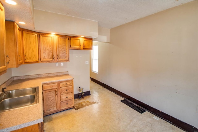 kitchen with brown cabinetry, baseboards, visible vents, a sink, and light countertops