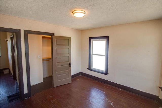 unfurnished bedroom featuring visible vents, baseboards, a textured ceiling, and dark wood-style floors