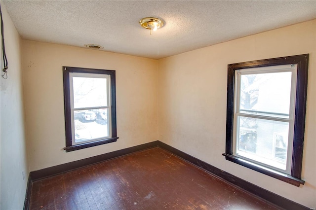 spare room with baseboards, plenty of natural light, dark wood-style floors, and a textured ceiling