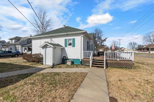 view of front facade with a wooden deck, a front yard, and a shingled roof