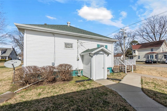 rear view of house with a yard, an outbuilding, a shingled roof, and a shed