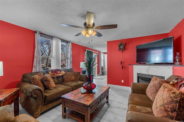 living room featuring baseboards, a fireplace, marble finish floor, a textured ceiling, and a ceiling fan