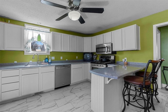 kitchen with marble finish floor, a sink, a textured ceiling, appliances with stainless steel finishes, and a peninsula