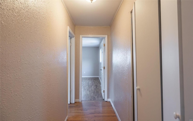 corridor with wood finished floors, a textured wall, and baseboards