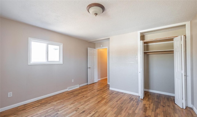 unfurnished bedroom featuring wood finished floors, baseboards, visible vents, a closet, and a textured ceiling