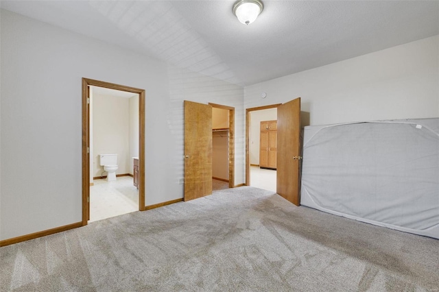 unfurnished bedroom with ensuite bathroom, a closet, carpet floors, baseboards, and a spacious closet