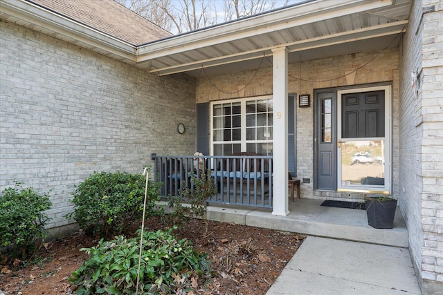 view of exterior entry featuring brick siding and covered porch