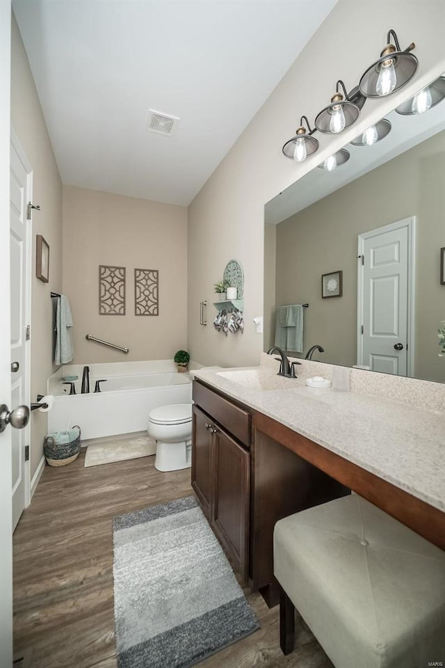 full bathroom with visible vents, a garden tub, toilet, wood finished floors, and vanity