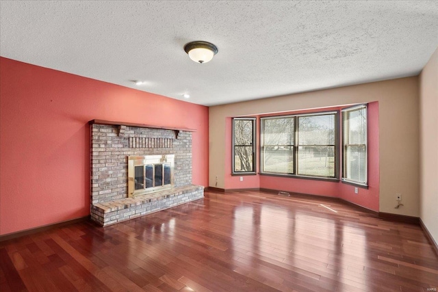 unfurnished living room with baseboards, a textured ceiling, a brick fireplace, and wood finished floors