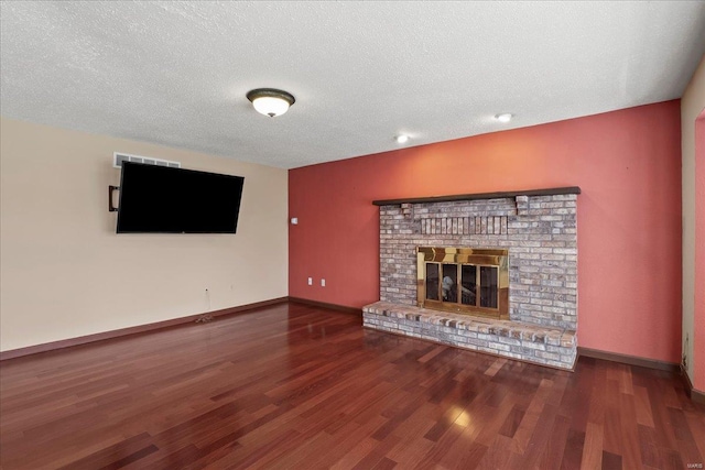 unfurnished living room featuring visible vents, a textured ceiling, wood finished floors, baseboards, and a brick fireplace