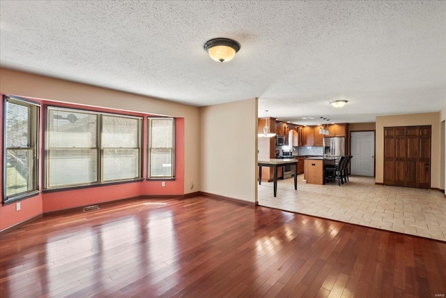 unfurnished living room with visible vents, baseboards, light wood-style floors, and a textured ceiling