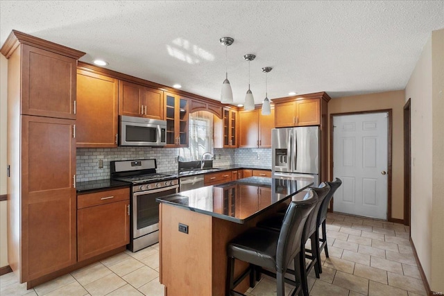 kitchen with dark countertops, a kitchen island, a breakfast bar, brown cabinetry, and stainless steel appliances