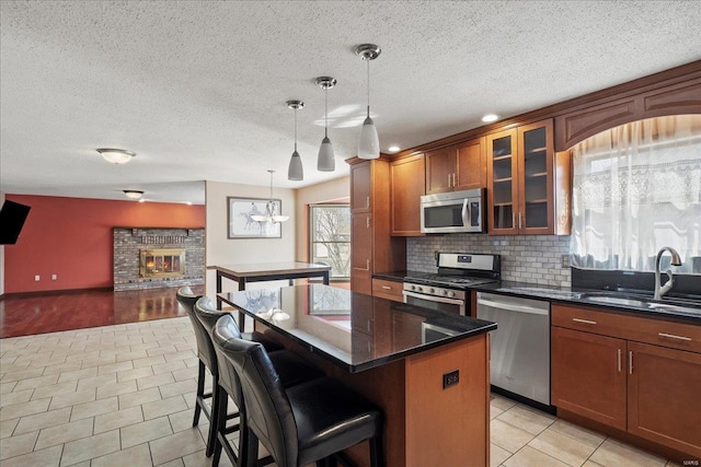 kitchen featuring a kitchen island, a fireplace, a sink, appliances with stainless steel finishes, and tasteful backsplash