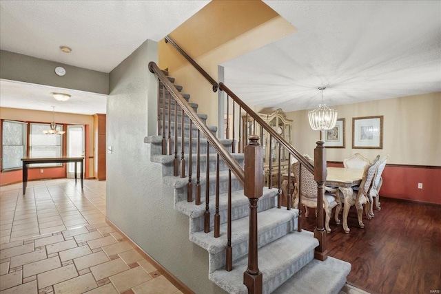 stairway with baseboards, a textured ceiling, an inviting chandelier, and wood finished floors