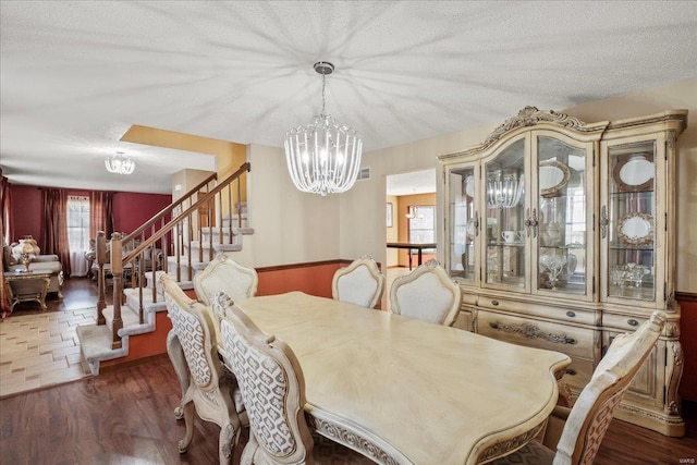 dining space featuring stairway, a textured ceiling, an inviting chandelier, and wood finished floors