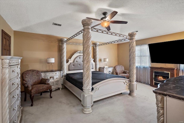 bedroom featuring ceiling fan, visible vents, light carpet, and a glass covered fireplace