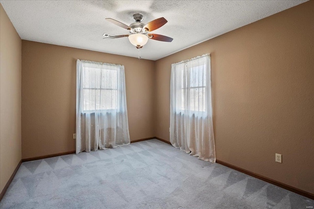 carpeted empty room with ceiling fan, baseboards, a wealth of natural light, and a textured ceiling