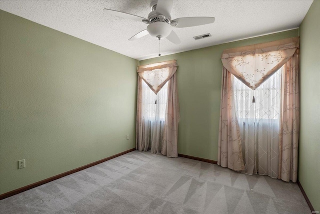 empty room featuring carpet flooring, a healthy amount of sunlight, a textured ceiling, and visible vents