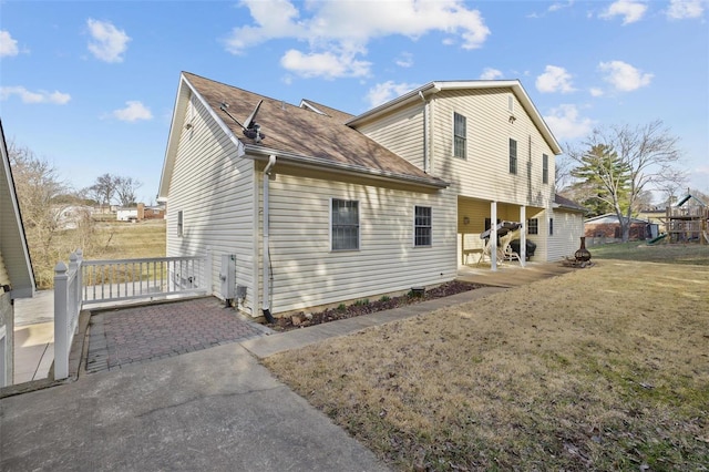 back of house with a yard, a patio area, and roof with shingles