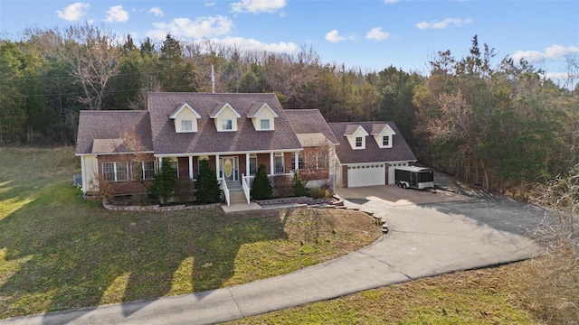 cape cod home with a front yard, a wooded view, covered porch, concrete driveway, and brick siding