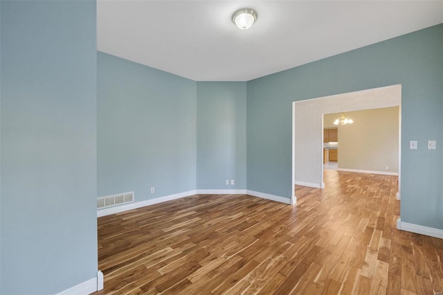 spare room featuring an inviting chandelier, wood finished floors, visible vents, and baseboards