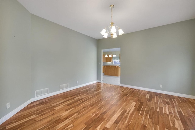 spare room with a notable chandelier, baseboards, visible vents, and light wood-type flooring