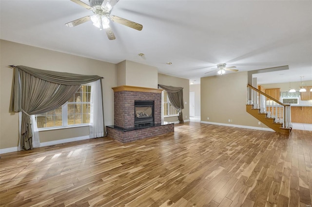 unfurnished living room with ceiling fan, stairway, wood finished floors, and a fireplace