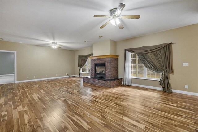 unfurnished living room with a fireplace, baseboards, ceiling fan, and wood finished floors