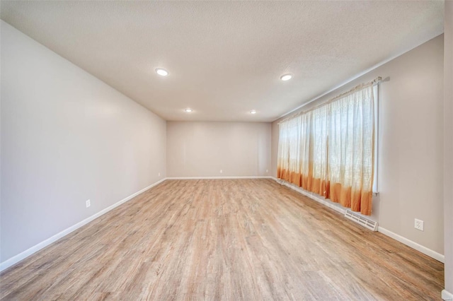 empty room featuring light wood-type flooring, visible vents, a textured ceiling, recessed lighting, and baseboards