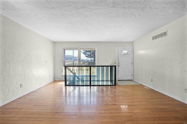 empty room with visible vents, a textured ceiling, wood finished floors, baseboards, and a textured wall