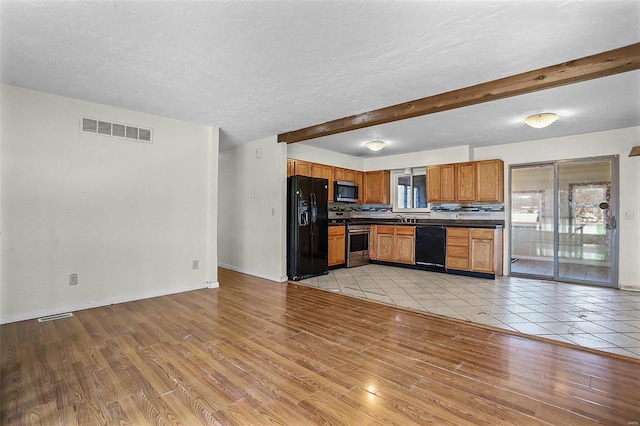 kitchen featuring dark countertops, visible vents, beam ceiling, light wood-style floors, and black appliances