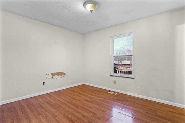 empty room with a textured ceiling, wood finished floors, visible vents, and baseboards