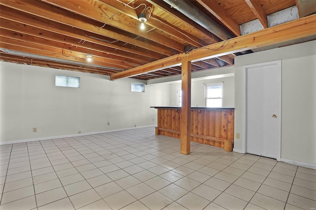 below grade area with a dry bar, light tile patterned flooring, baseboards, and plenty of natural light