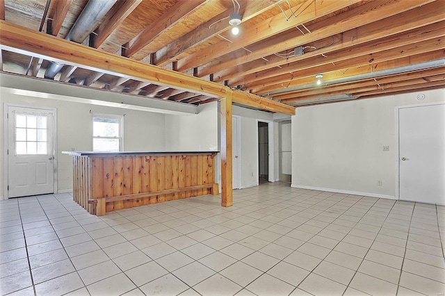 below grade area featuring baseboards, a bar, and light tile patterned flooring