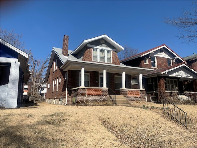 view of front facade with covered porch, brick siding, and a chimney