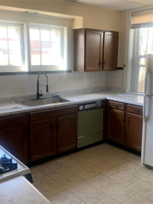 kitchen featuring a sink, tasteful backsplash, freestanding refrigerator, dishwasher, and a healthy amount of sunlight