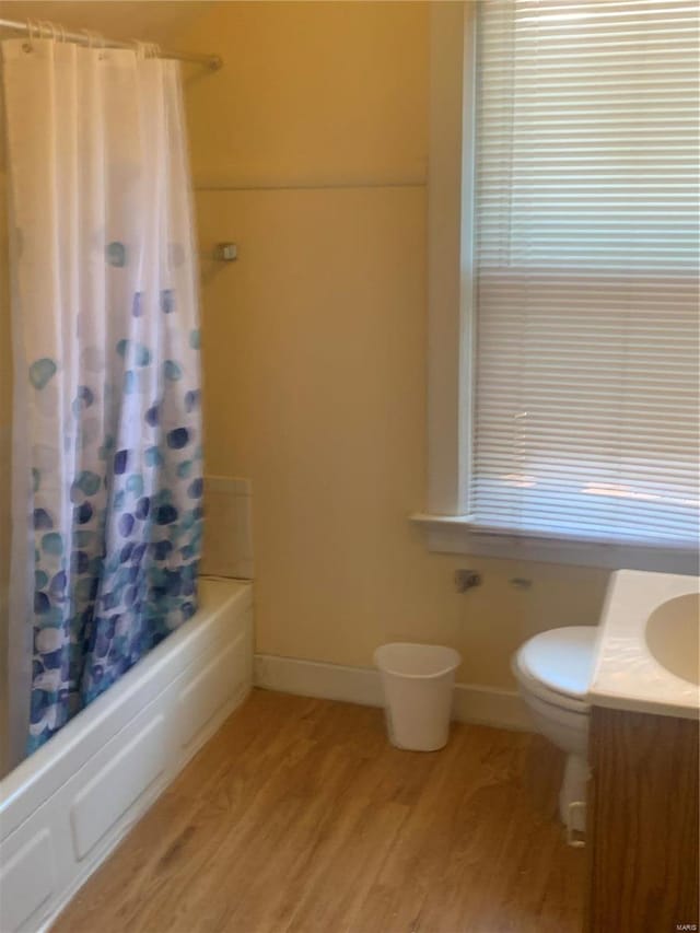 bathroom featuring vanity, wood finished floors, baseboards, shower / bath combo with shower curtain, and toilet