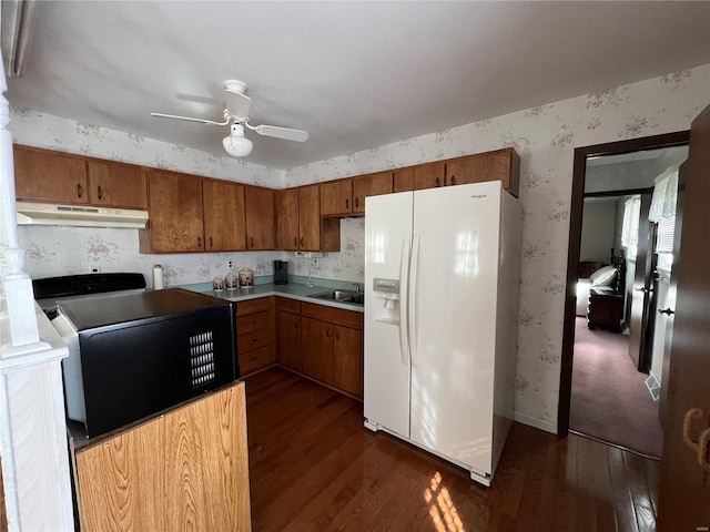 kitchen featuring under cabinet range hood, brown cabinets, white refrigerator with ice dispenser, and wallpapered walls