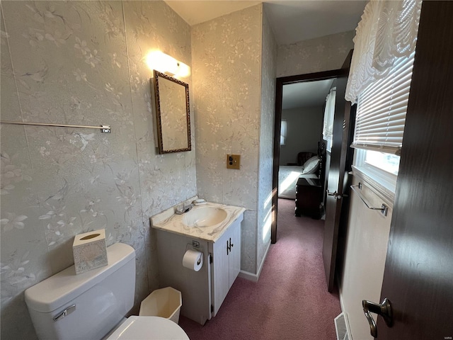 half bath with toilet, wallpapered walls, and vanity