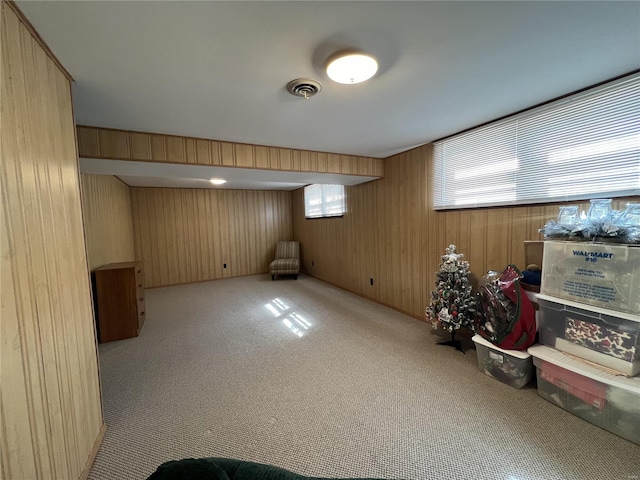 basement featuring wooden walls, carpet flooring, and visible vents